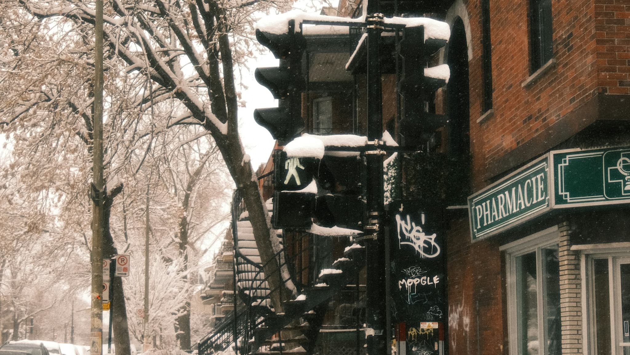 A snowy street corner in Montreal, with a pharmacy and an outdoor spiral staircase.